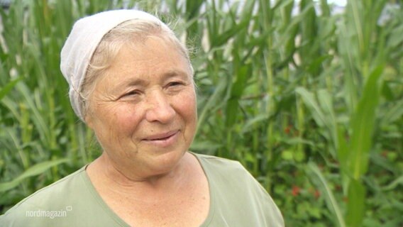 Eine Dame mit Kopftuch vor Pflanzen guckt zufrieden in die Kamera. © Screenshot 