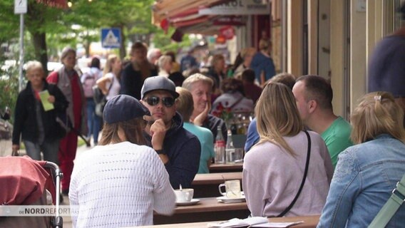 Menschen sitzen vor einem Restaurant. © Screenshot 
