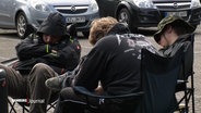Schlafende Wacken-Fans auf Campingstühlen auf einem Parkplatz. © Screenshot 