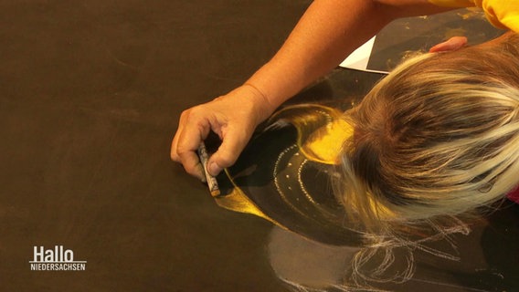 Eine Künstlerin malt ein Bild auf einen Boden. © Screenshot 