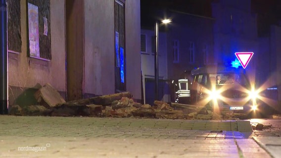 Nächtliche Straßenszene: Im Vordergrund Steine und Mauerreste, im Hintergrund ein Fahrzeug der Polizei mit eingeschalteten Scheinwerfern und Blaulicht. © Screenshot 