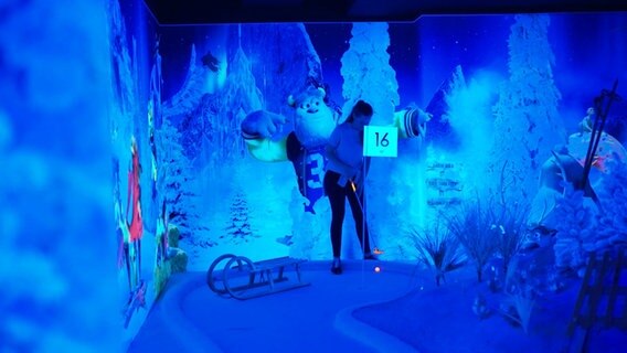 Indoor-Minigolf-Spielerin in blauem Licht. © Screenshot 