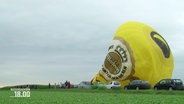 Ein in sich zusammengefallener Heißluftballon liegt auf einem Feld. © Screenshot 