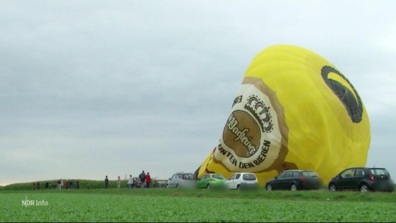 Ein in sich zusammengefallener Heißluftballon liegt auf einem Feld. © Screenshot 