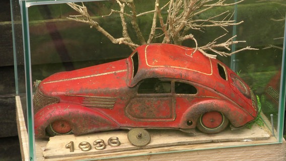 Rotes Modellauto in einer Glasvitrine. © Screenshot 