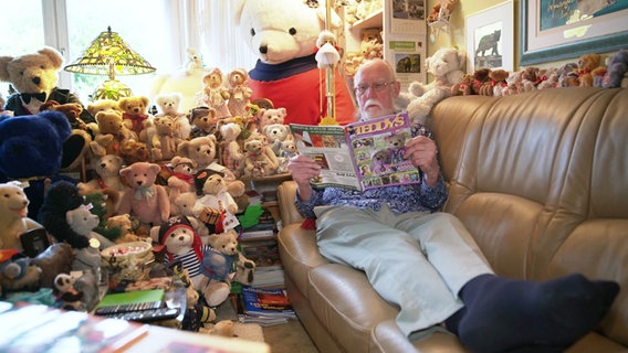 Ein Mann sitzt auf einem Sofa, umrahmt von vielen Teddys. © Screenshot 