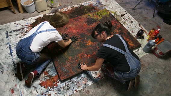 Von oben betrachtet: Marta Jansana und Frauke Kohlmorgen malen in ihrem Atelier gemeinsam. Das Bild liegt dafür auf dem Boden, die Künstlerinnen arbeiten mit ihren Händen, ohne Pinsel. © Screenshot 