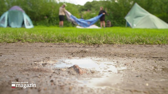 Eine Pfütze vor einem nassen Zeltplatz. © Screenshot 