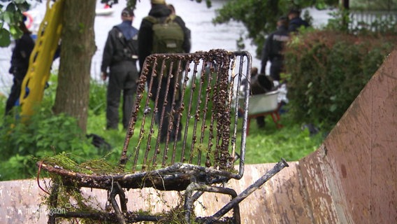 Ein verrosteter Metallstuhl, im Hintergrund Polizisten. © Screenshot 