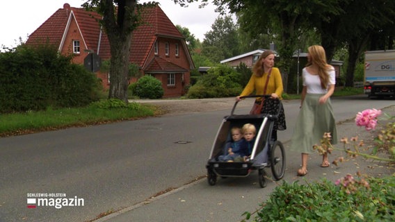 Zwei Frauen laufen mit Kinderwagen an einer vielbefahrenen Straße entlang. © Screenshot 