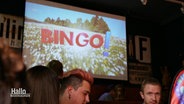 Eine Leinwand in der Dorfkneipe "Zum Amtsschimmel" auf dem BINGO! übertragen wird. © Screenshot 