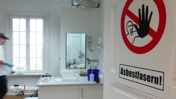 Blick in ein Labor; an der offenen Tür kleben Warnschilder bzgl. Asbestfasern. © Screenshot 