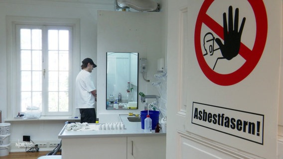 Blick in ein Labor; an der offenen Tür kleben Warnschilder bzgl. Asbestfasern. © Screenshot 