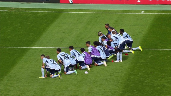 Die Spieler des HSV knien auf dem Rasen. © Screenshot 