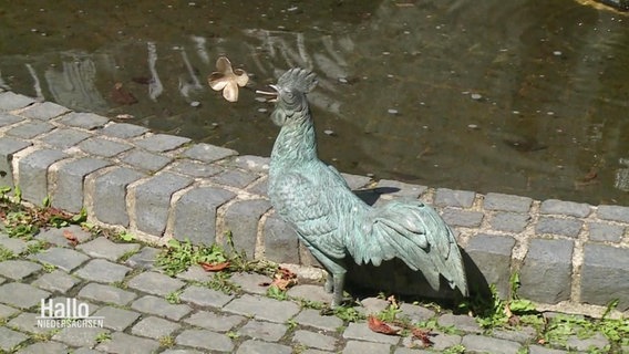 Eine Hahnenskulptur mit einem goldenen KIeeblatt im Schnabel. © Screenshot 
