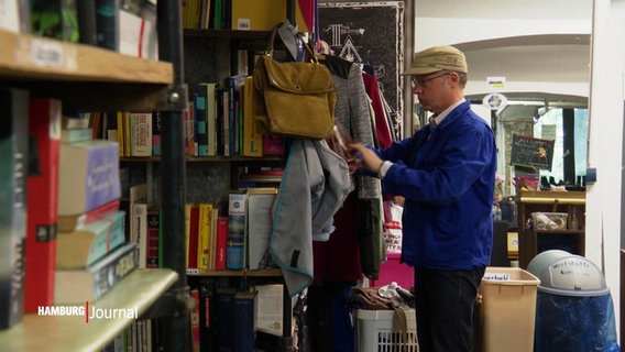Ein Mann sortiert Kleidungsstücke in einem Umsonstladen. © Screenshot 