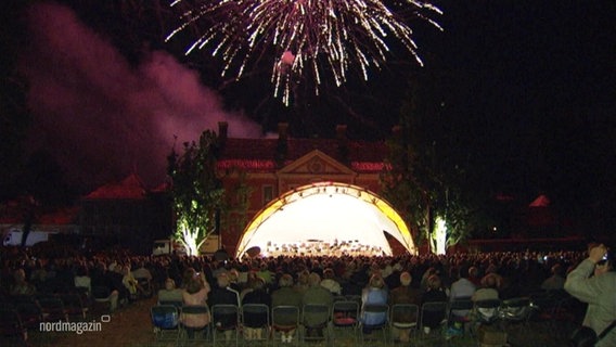 Blick über die Zuschauer hin zur Bühne beim Freiluftkonzert auf Schloss Bothmer mit Feuerwerk. © Screenshot 