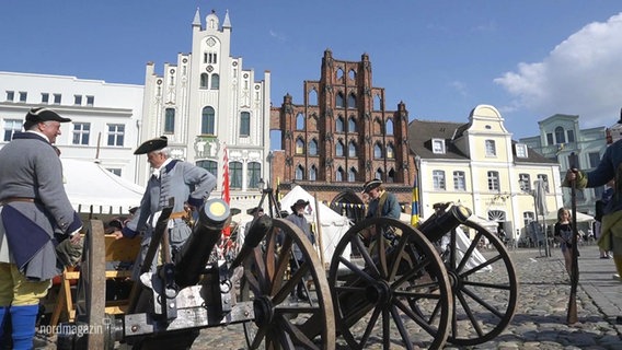 Männer in historischer Kluft stehen auf dem Markplatz in Wismar. Vor ihnen zwei alte Kanonen. © Screenshot 