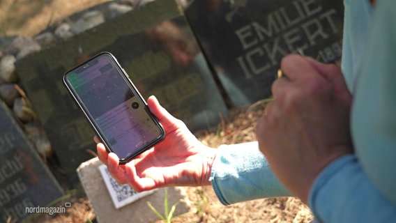 Eine Person scannt einen QR-Code auf einem Friedhof mit ihrem Smartphone. © Screenshot 