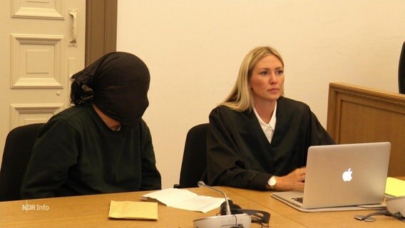 Ein Angeklagter hat vor Gericht sein Gesicht mit einem schwarzen Tuch verhüllt. © Screenshot 