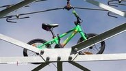Ein grünes Kinderfahrrad ist an einen Strommast befestigt. © Screenshot 