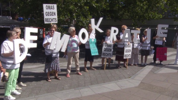 Ältere Damen halten die Buchstaben des Wortes "Demokratie" hoch, dazu ein Schilder mit der Aufschrift "OMAS GEGEN RECHTS". © Screenshot 