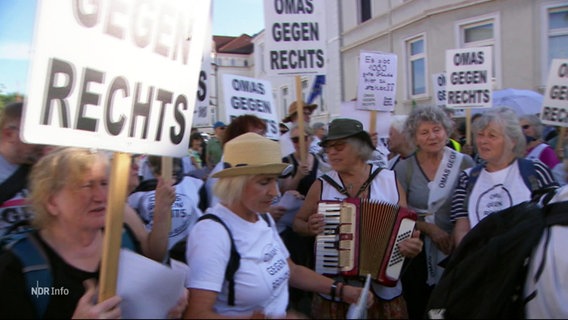 Mehrere ältere Damen protestieren gegen Rechtspopulisten, eine spielt ein Akkordeon. © Screenshot 