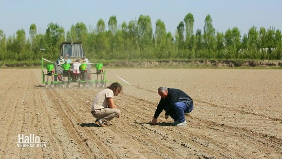 Zwei Personen untersuchen den Boden eines Ackers, ein Traktor pflügt im Hintergrund. © Screenshot 