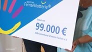 Nahaufnahme von einem symbolischen Check der Deutschen Fernsehlotterie in Höhe von 99.000 Euro. © Screenshot 