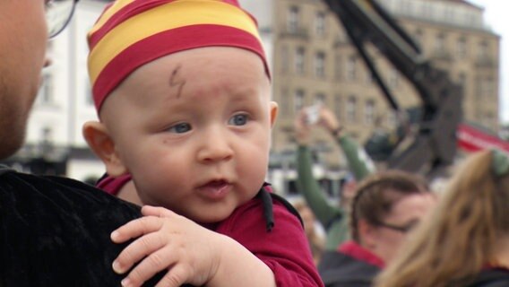 Ein Baby auf dem Arm mit einer aufgemalten Blitz-Narbe im Stile von Harry Potter © Screenshot 