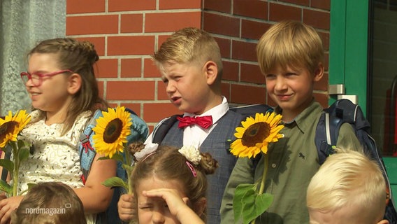 Frisch eingeschulte Kinder halten Sonnenblumen. © Screenshot 