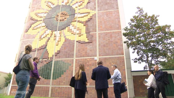 Menschen stehen vor dem Sonnenblumenhaus in Lichtenhagen. © Screenshot 