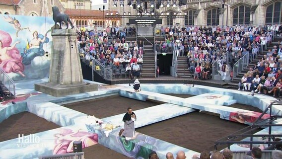 Freilicht-Inszenierung von "Tosca" auf dem Burgplatz: Das Publikum sitzt in einer Arena um ein ringförmiges Bühnenbild mit Stegen durch die Mitte. © Screenshot 