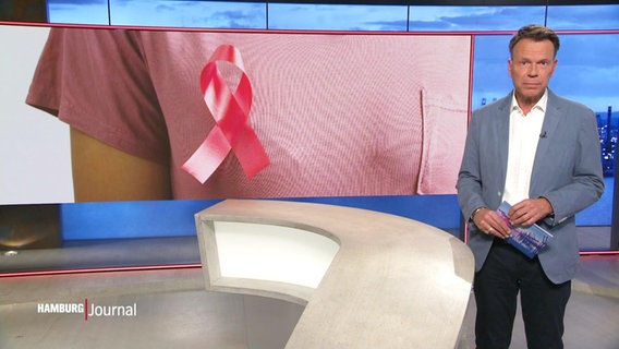 Nachrichtensprecher Ulf Ansorge, im Hintergrund ein Bild von einer Krebs-Gedenk-Ansteckschleife an einem T-Shirt. © Screenshot 