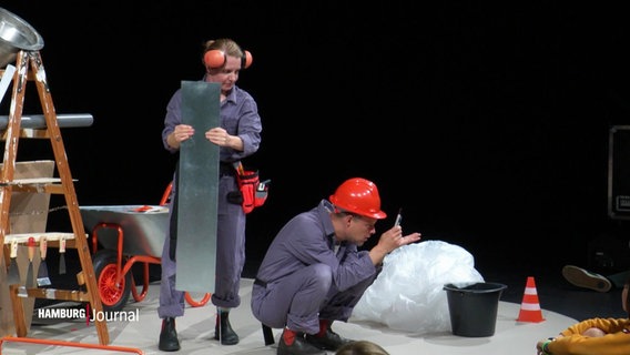 Zwei als Bauarbeiter verkleidete Schauspielende auf einer Bühne. © Screenshot 