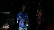 Menschen stehen in der Dunkelheit in der Natur. Sie schauen nach oben gen Himmel, ein Mann hält eine Taschenlampe. Ein Mädchen hält einen Sensor nach oben. © Screenshot 