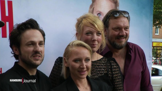 Drei Schauspielende und Charlie Hübner stehen vor einem Filmplakat für ein Fotoshooting nebeneinander. © Screenshot 