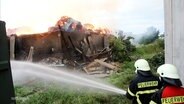 Feuerwehrleute löschen eine brennende Lagerhalle. © Screenshot 