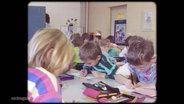Ein altes Foto von schreibenden Kindern in einem Klassenzimmer. © Screenshot 