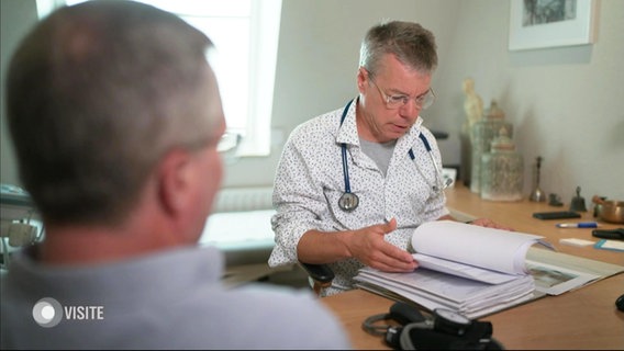 Ein Arzt sieht eine Akte ein, ein Patient sitzt im Vordergrund. © Screenshot 