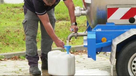 Ein Mann füllt Wasser in einen Kanister ab. © Screenshot 