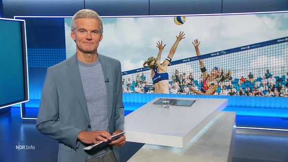Nachrichtensprecher Thorsten Schröder, im Hintergrund ein Bild von einem Beachvolleyballspiel. © Screenshot 