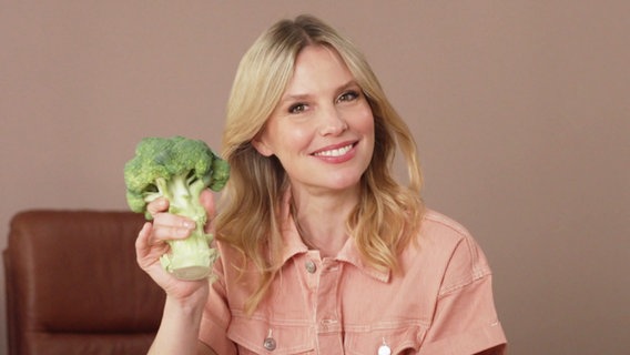 Dr. Julia hält eine Brokkoli in der Hand und lächelt in die Kamera. © Screenshot 
