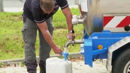 Ein Mann füllt Wasser aus einem Tank in einen Kanister. © Screenshot 
