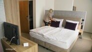 Eine Frau macht ein Bett in einem Hotelzimmer. © Screenshot 