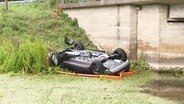 Ein Auto liegt neben einer Brücke auf dem Dach. © Screenshot 