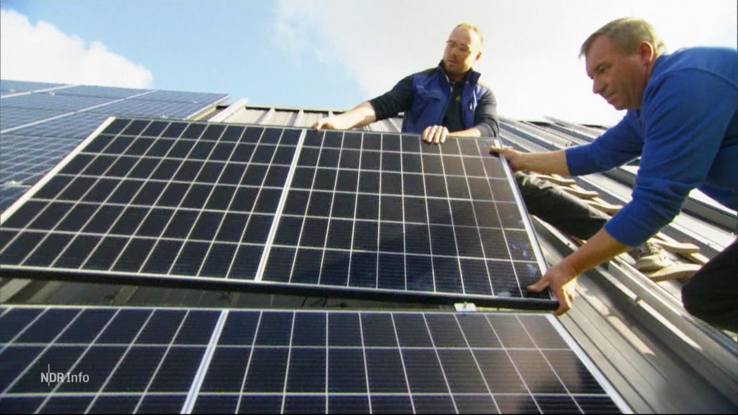 Zwei Personen installieren Solaranlagen auf einem Dach.