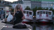 Eine junge Frau sitzt telefonierend an der Hamburger Alster. © Screenshot 