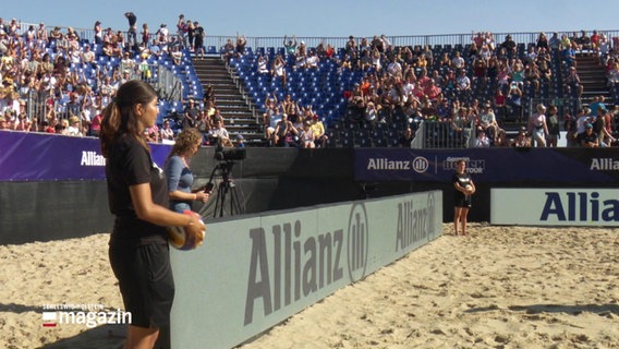 Zwei junge Frauen stehen am Rande eines Beachvolleyball-Feldes. © Screenshot 