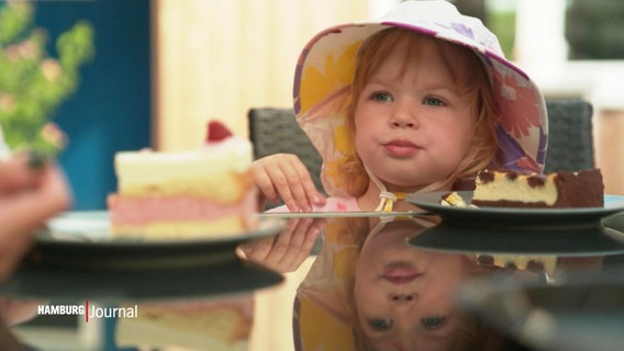 Ein kleines Mädchen sitzt in einem Café am Tisch und blickt auf Kuchen. © Screenshot 
